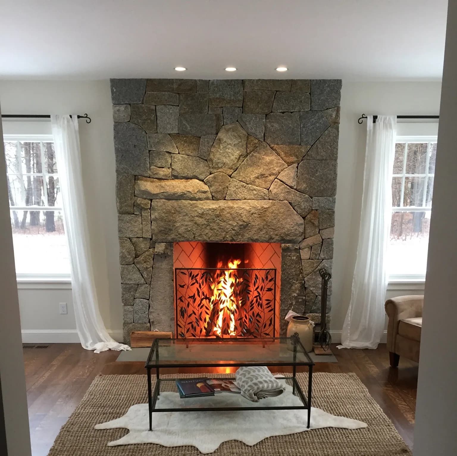 Floor-to-ceiling fieldstone fireplace with a stone lintel and herringbone firebrick firebox, fire burning in a living room