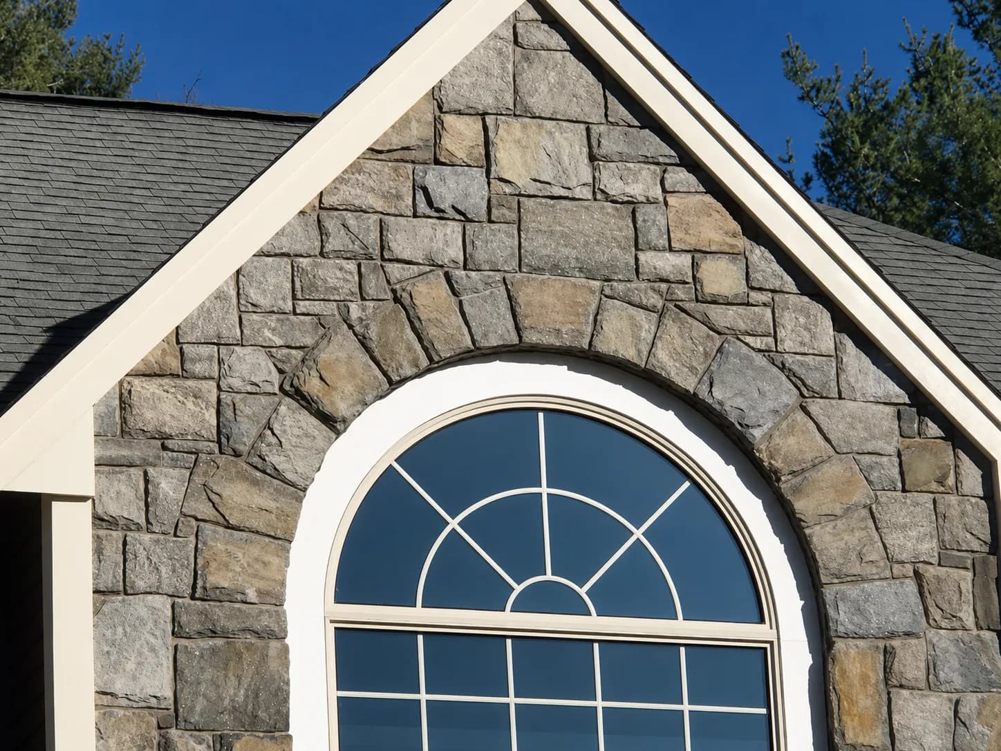 Granite stone veneer gable wrapping a Roman arch window on a residential home