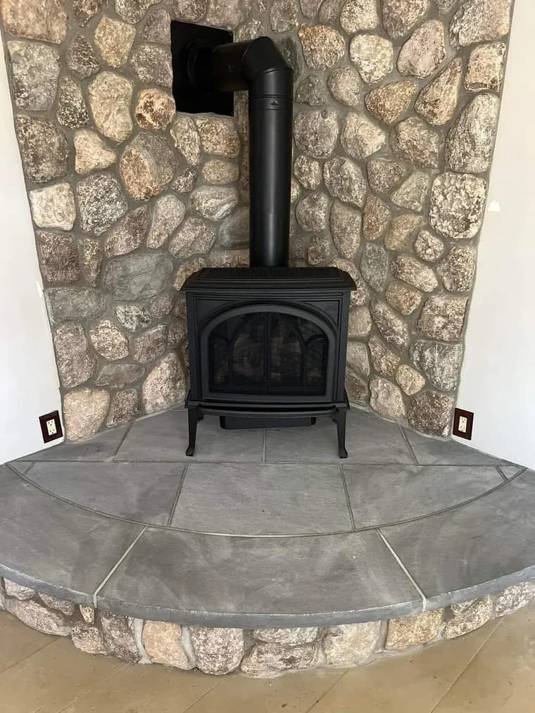 Wood stove against an irregular fieldstone fireplace wall on a curved gray slab hearth