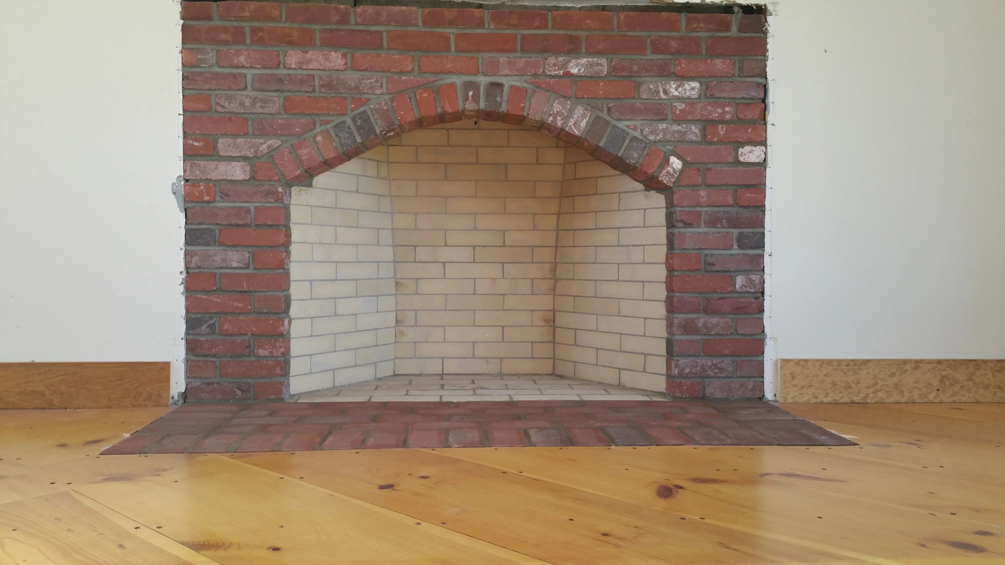 Custom brick fireplace with a curved arch and firebrick-lined firebox in a home under renovation