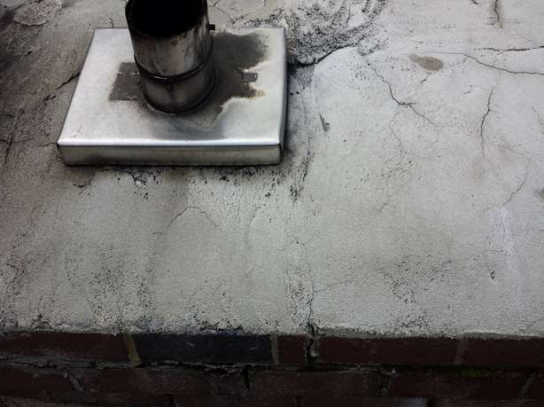 Cracked chimney crown around a metal flue showing surface deterioration
