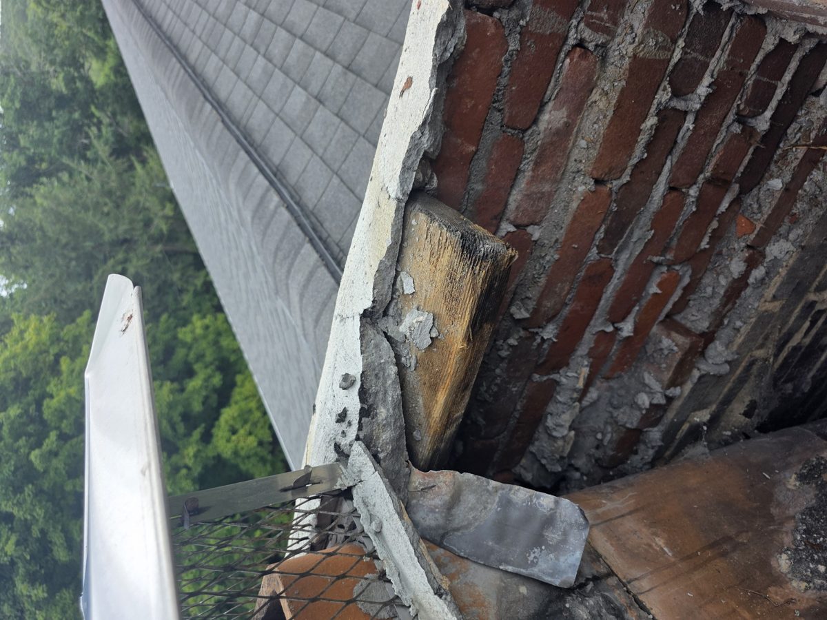 Failed thin chimney crown broken apart above hidden wood and deteriorated brick