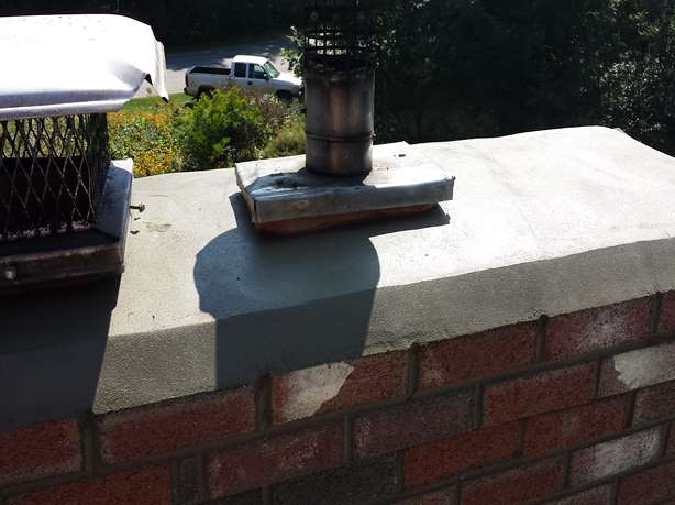 Newly rebuilt chimney crown with a sloped cement surface protecting a brick chimney